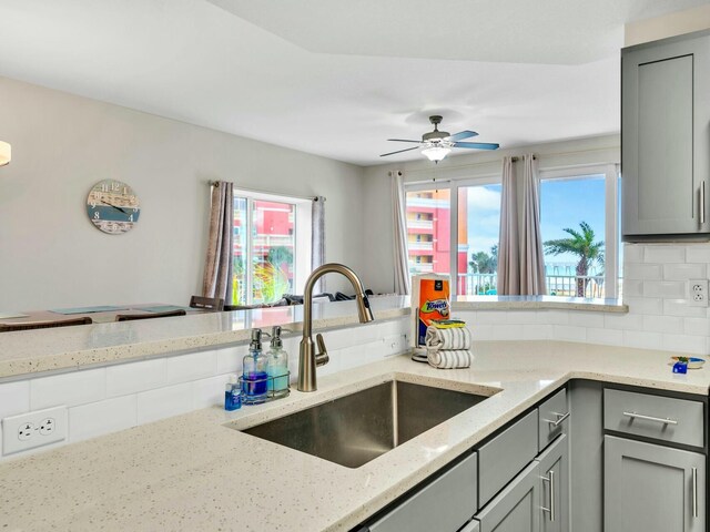 kitchen featuring decorative backsplash, light stone countertops, gray cabinetry, ceiling fan, and sink