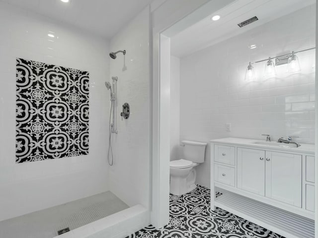 bathroom featuring tile walls, toilet, a sink, tiled shower, and tile patterned floors