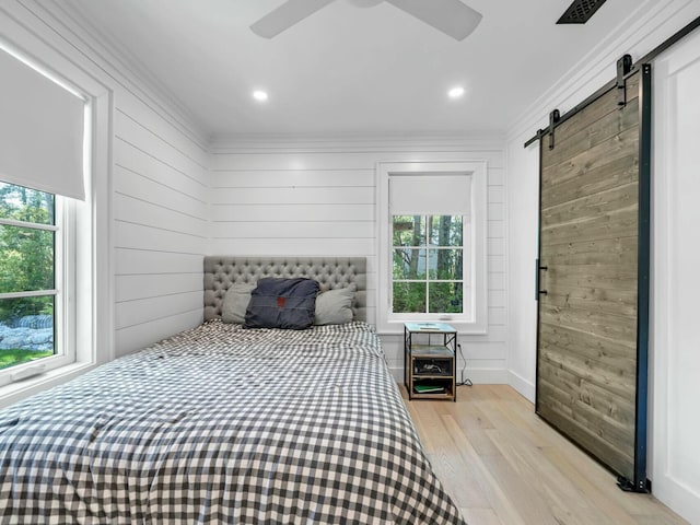 bedroom with a barn door, multiple windows, light wood-style floors, and crown molding