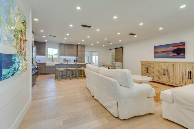 living room with light wood-type flooring, a barn door, visible vents, and recessed lighting