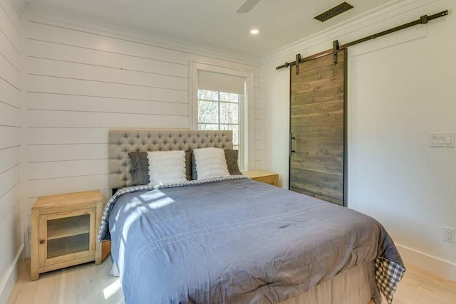 bedroom featuring a barn door, visible vents, light wood-style flooring, and crown molding