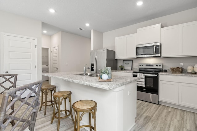 kitchen featuring white cabinets, stainless steel appliances, sink, a kitchen island with sink, and a breakfast bar