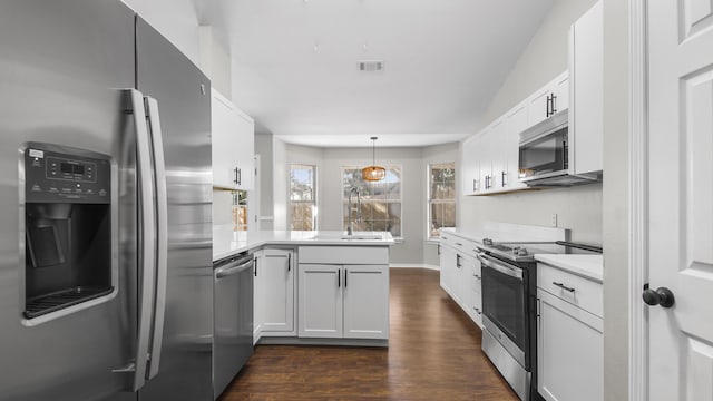 kitchen with kitchen peninsula, appliances with stainless steel finishes, sink, decorative light fixtures, and white cabinetry