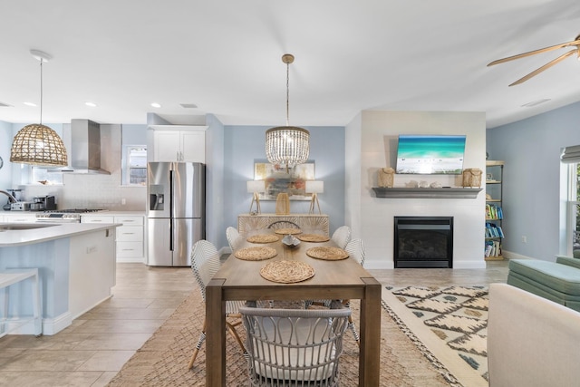 interior space with pendant lighting, white cabinets, stainless steel fridge with ice dispenser, and wall chimney exhaust hood