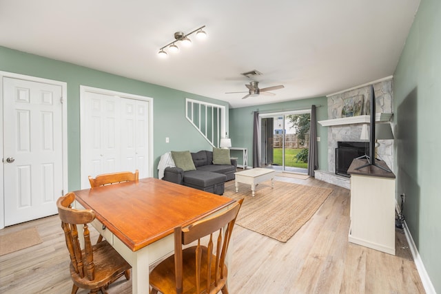 dining room with track lighting, light hardwood / wood-style floors, a stone fireplace, and ceiling fan