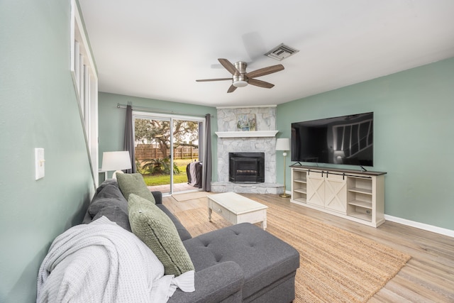 living room featuring ceiling fan, a stone fireplace, and wood-type flooring