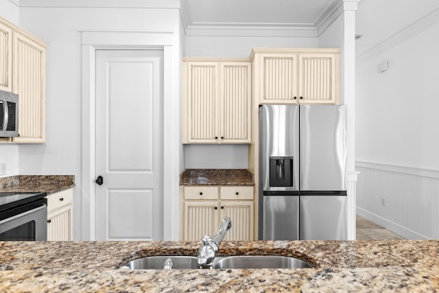 kitchen with cream cabinets, sink, dark stone countertops, ornamental molding, and appliances with stainless steel finishes