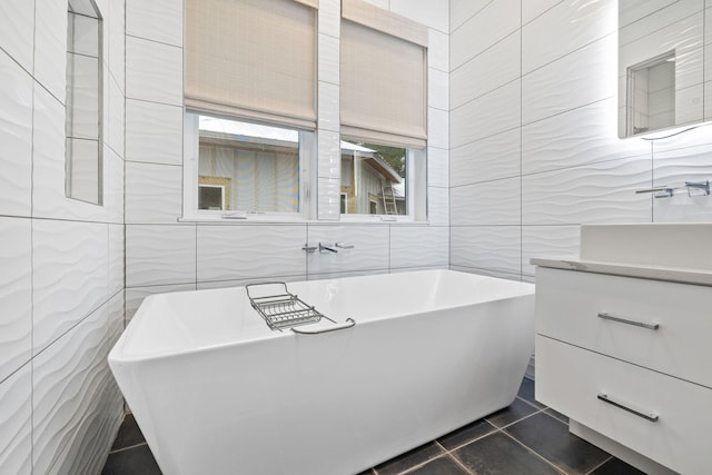 bathroom with tile walls, vanity, tile patterned floors, and a tub to relax in