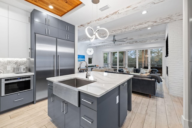 kitchen with ceiling fan, white cabinetry, hanging light fixtures, stainless steel appliances, and an island with sink