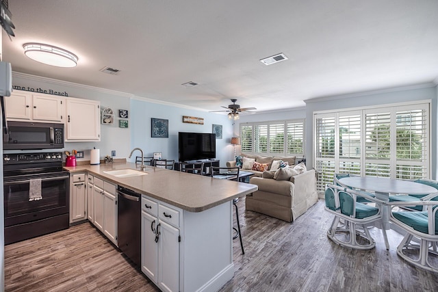 kitchen featuring black appliances, a breakfast bar, kitchen peninsula, sink, and white cabinets