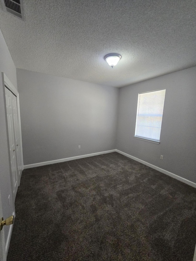 unfurnished room featuring a textured ceiling and dark colored carpet