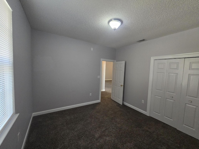 unfurnished bedroom featuring dark carpet, multiple windows, a textured ceiling, and a closet