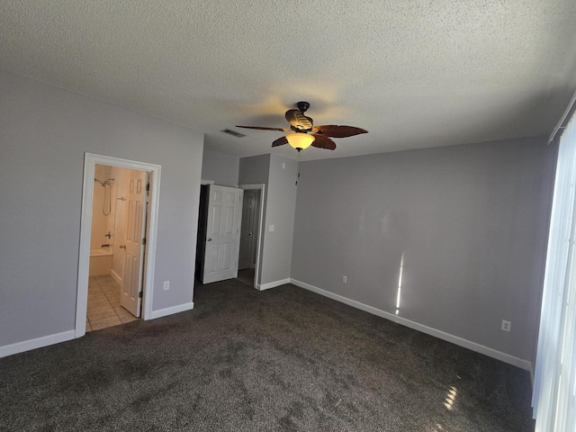 unfurnished bedroom featuring a textured ceiling, ensuite bathroom, dark carpet, and ceiling fan