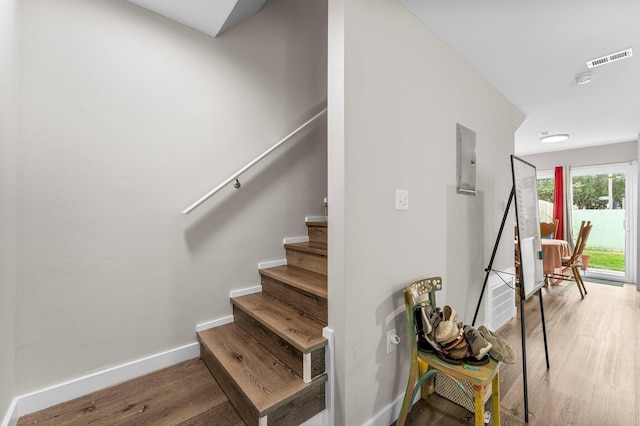 stairway with electric panel and hardwood / wood-style floors