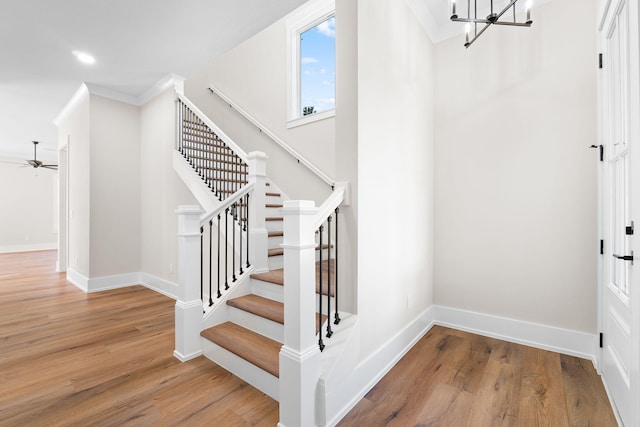 stairs featuring hardwood / wood-style floors, ceiling fan with notable chandelier, and ornamental molding