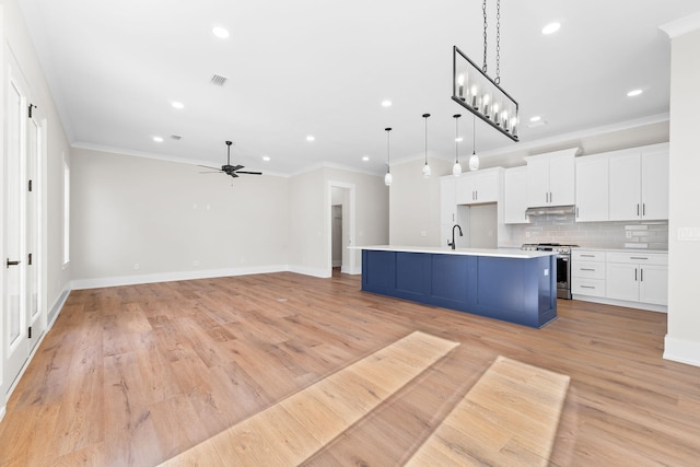 kitchen with gas range, white cabinetry, tasteful backsplash, decorative light fixtures, and a center island with sink