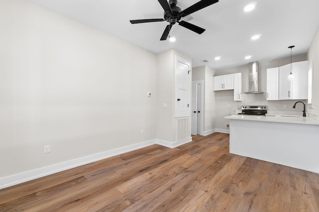 kitchen featuring stainless steel electric range oven, wall chimney range hood, light hardwood / wood-style floors, decorative light fixtures, and white cabinets