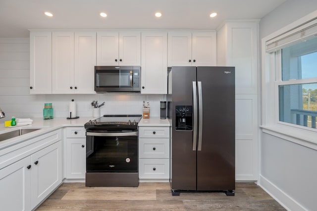 kitchen featuring white cabinets, light wood-type flooring, stainless steel appliances, and tasteful backsplash