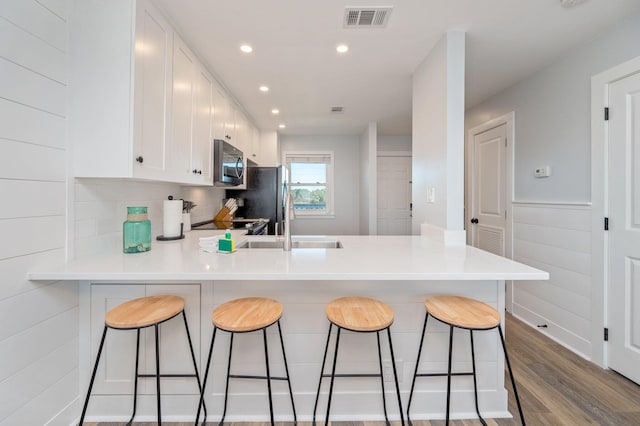 kitchen featuring white cabinetry, a kitchen breakfast bar, kitchen peninsula, hardwood / wood-style floors, and appliances with stainless steel finishes