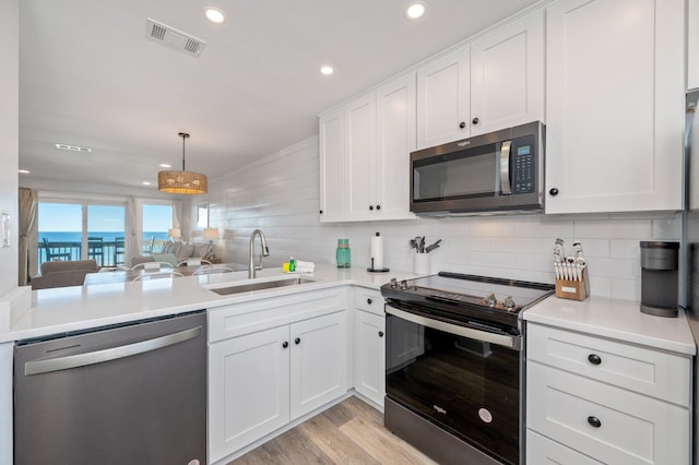 kitchen with white cabinetry, sink, stainless steel appliances, pendant lighting, and light wood-type flooring