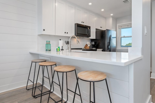 kitchen featuring white cabinets, kitchen peninsula, a breakfast bar area, and refrigerator with ice dispenser