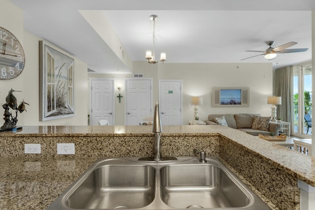 kitchen featuring ceiling fan with notable chandelier, stone countertops, hanging light fixtures, and sink