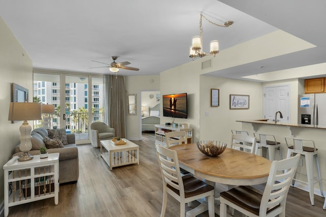 dining space with ceiling fan with notable chandelier, expansive windows, sink, and light hardwood / wood-style flooring