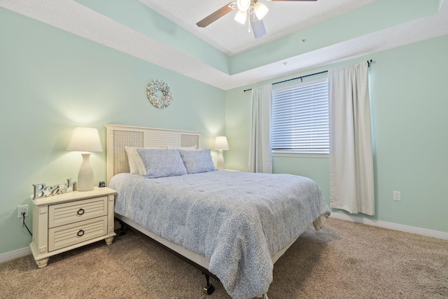 carpeted bedroom with a raised ceiling and ceiling fan