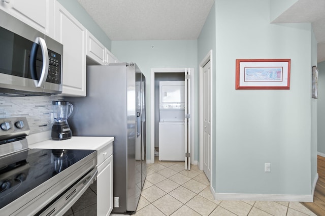 kitchen with white cabinetry, light tile patterned floors, stainless steel appliances, and stacked washer / drying machine