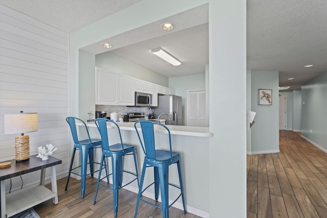 kitchen with a breakfast bar, white cabinets, hardwood / wood-style flooring, a textured ceiling, and appliances with stainless steel finishes