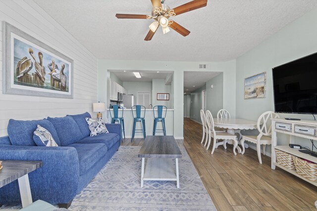 living room featuring ceiling fan, wooden walls, a textured ceiling, and hardwood / wood-style flooring