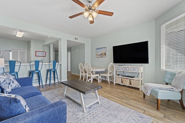 living room with a textured ceiling, light hardwood / wood-style flooring, and ceiling fan