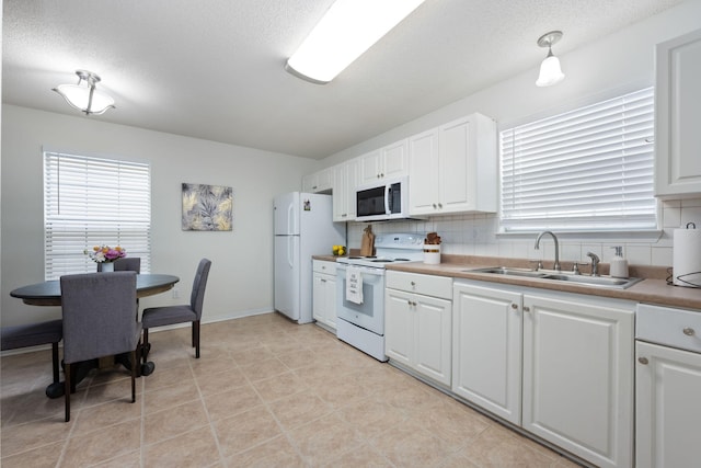 kitchen featuring sink, backsplash, white cabinets, plenty of natural light, and white appliances