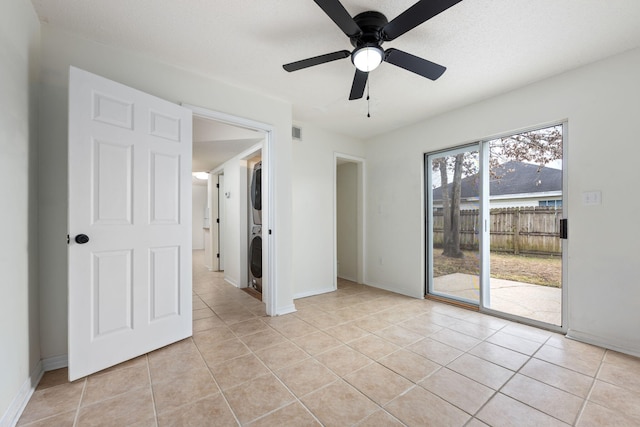 empty room featuring stacked washer and clothes dryer, light tile patterned floors, and ceiling fan