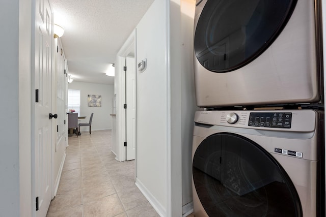 laundry area featuring light tile patterned floors, a textured ceiling, and stacked washing maching and dryer