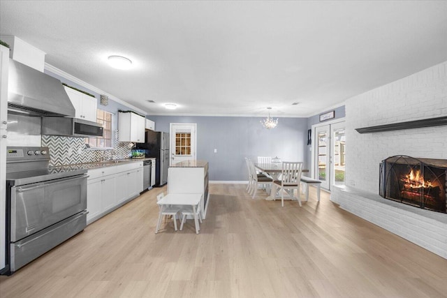 kitchen featuring backsplash, wall chimney range hood, a fireplace, white cabinetry, and stainless steel appliances