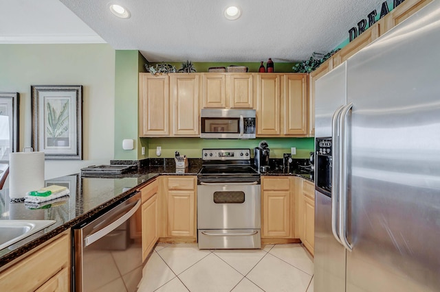 kitchen featuring light brown cabinets, dark stone counters, a textured ceiling, light tile patterned flooring, and appliances with stainless steel finishes