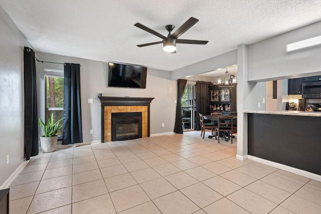 unfurnished living room with a fireplace, light tile patterned floors, a textured ceiling, baseboards, and ceiling fan with notable chandelier