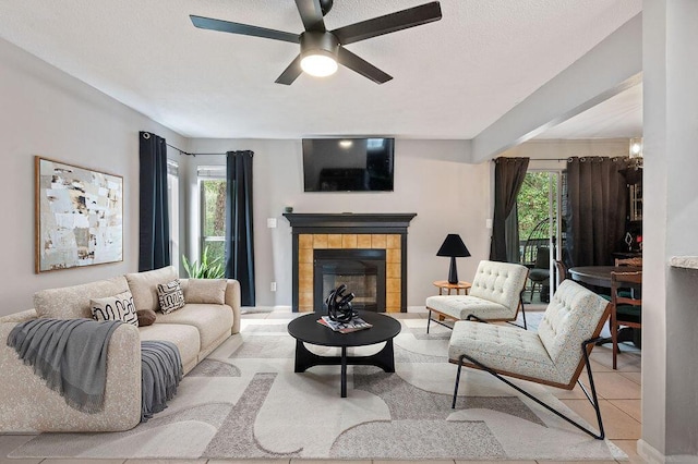 living area featuring a tiled fireplace, ceiling fan, plenty of natural light, and baseboards