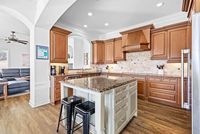 kitchen featuring a kitchen breakfast bar, custom exhaust hood, hardwood / wood-style flooring, stone counters, and a kitchen island