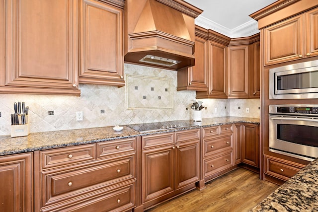 kitchen with custom range hood, backsplash, stainless steel appliances, and dark stone counters