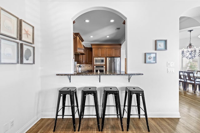 kitchen featuring a kitchen breakfast bar, stainless steel appliances, decorative light fixtures, and dark stone counters