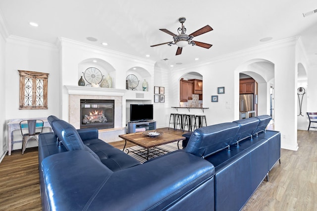 living room with ceiling fan, light hardwood / wood-style floors, ornamental molding, and a fireplace