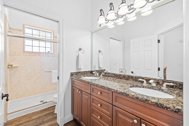 bathroom with vanity, tiled shower, hardwood / wood-style flooring, an inviting chandelier, and toilet