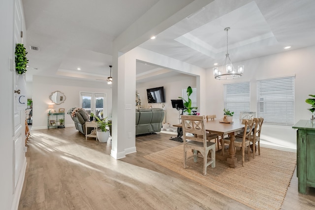 dining space with ceiling fan with notable chandelier, light hardwood / wood-style flooring, and a raised ceiling