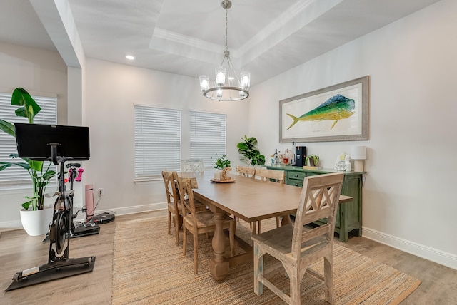 dining room featuring a raised ceiling, a chandelier, and light wood-type flooring