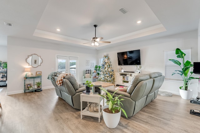 living room with light wood-type flooring, a tray ceiling, ceiling fan, and crown molding