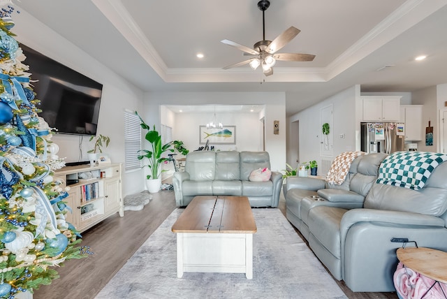 living room featuring ceiling fan with notable chandelier, ornamental molding, light hardwood / wood-style flooring, and a tray ceiling