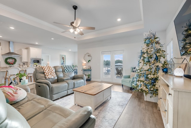 living room featuring a raised ceiling, ceiling fan, light hardwood / wood-style floors, and ornamental molding