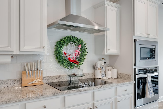 kitchen with white cabinetry, light stone countertops, wall chimney exhaust hood, stainless steel appliances, and backsplash